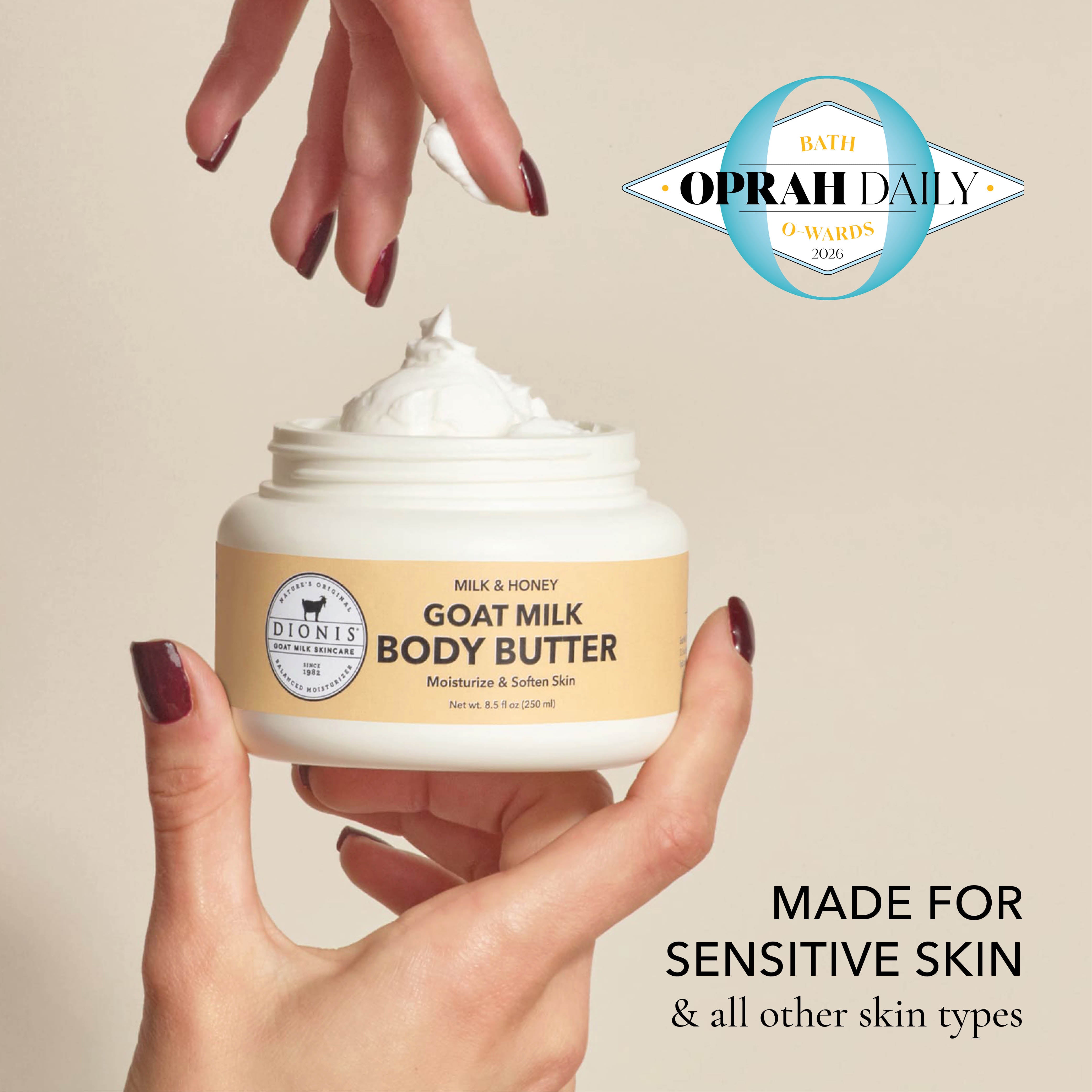 A hand holds an open jar of Dionis Goat Milk Body Butter in Milk & Honey, showing the white cream being dispensed. Another hand with dark burgundy nail polish is positioned above the jar.