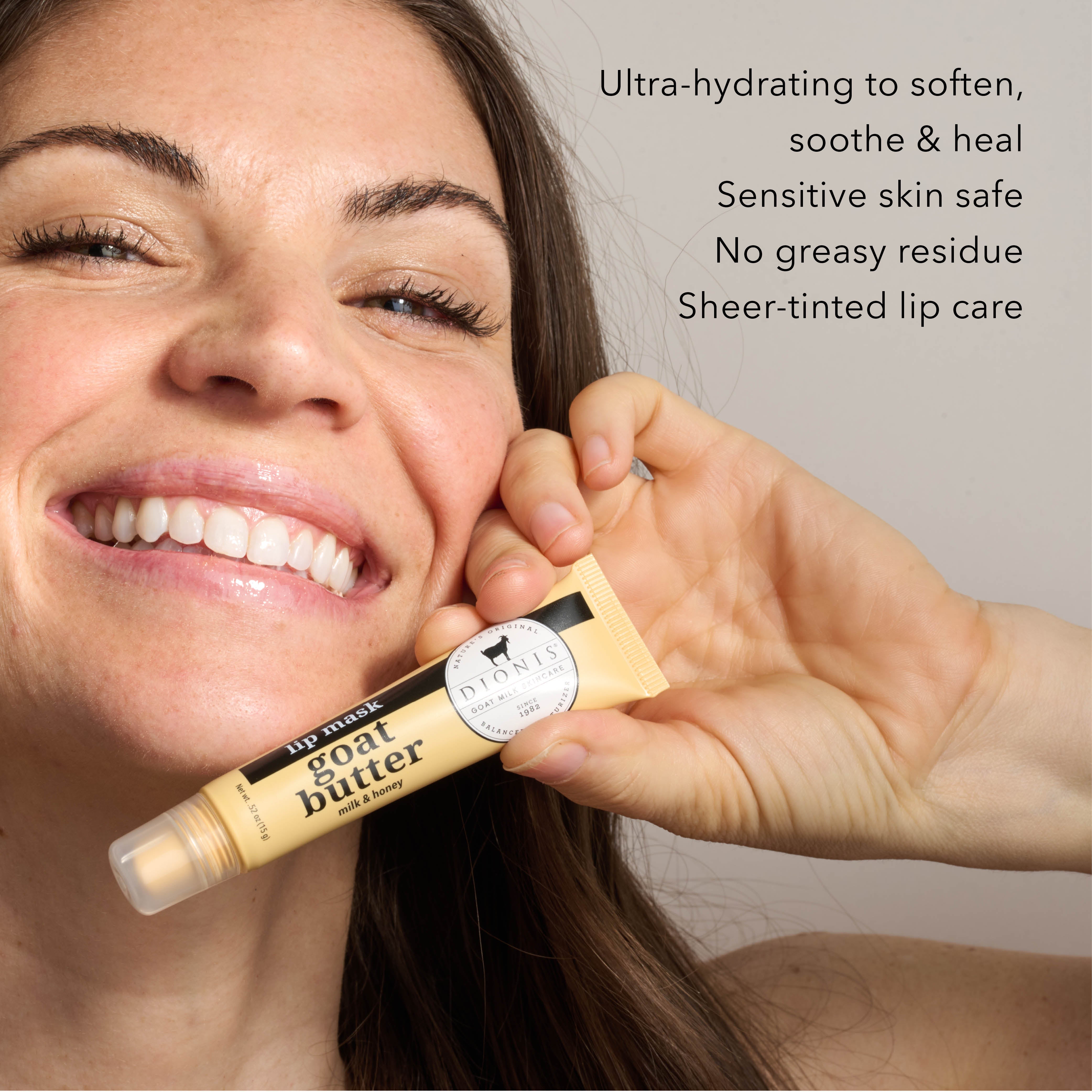 Woman holds up tube of Dionis Goat Butter Milk & Honey Lip Balm while smiling