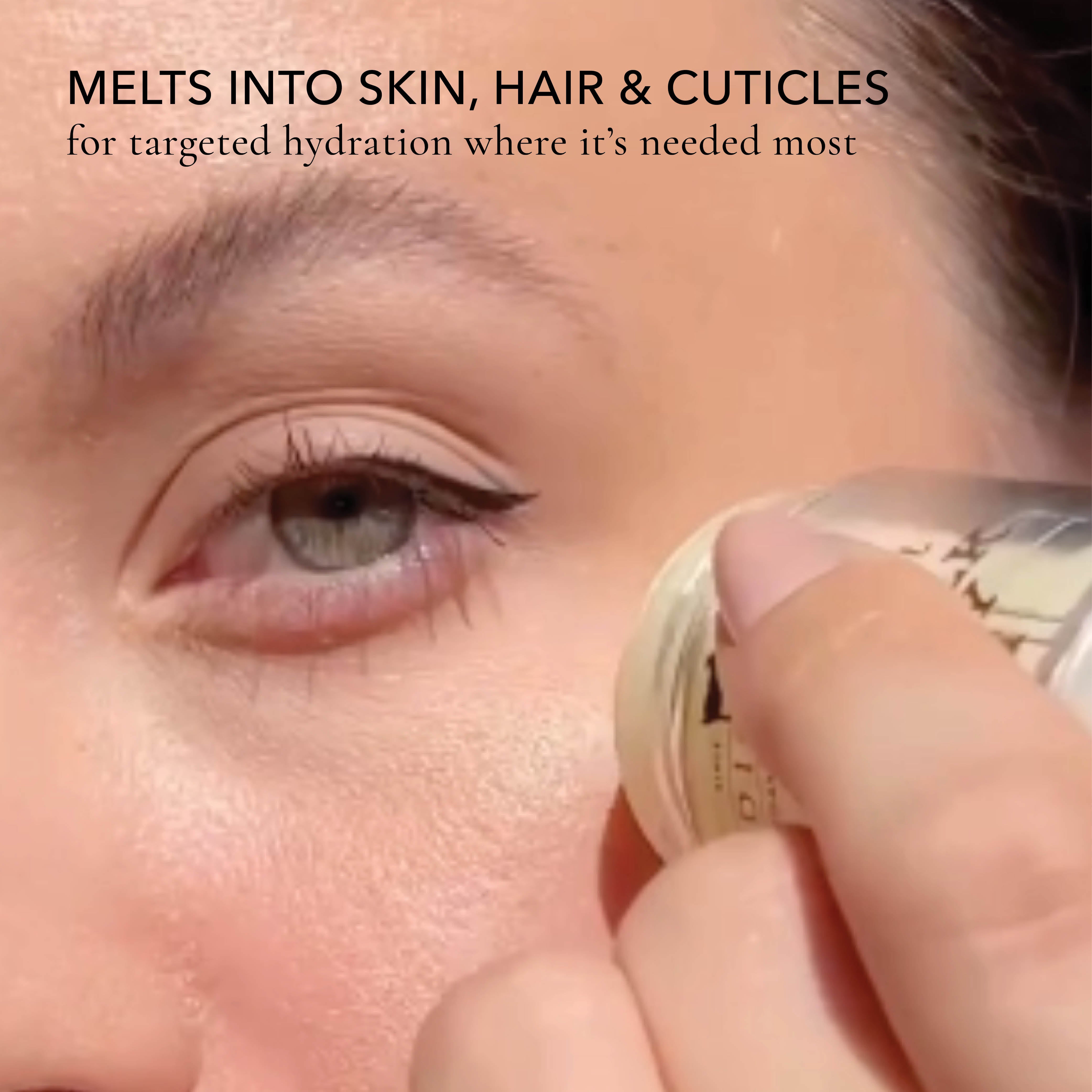 Close-up of a person applying a cosmetic product to their eye area, with text reading 'MELTS INTO SKIN, HAIR & CUTICLES for targeted hydration where it's needed most'.