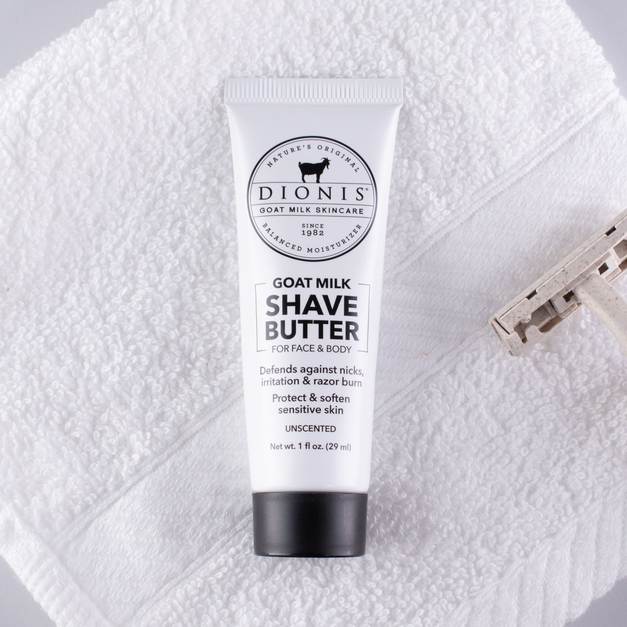 A tube of Dionis Goat Milk Shave Butter placed on a white towel next to a razor.