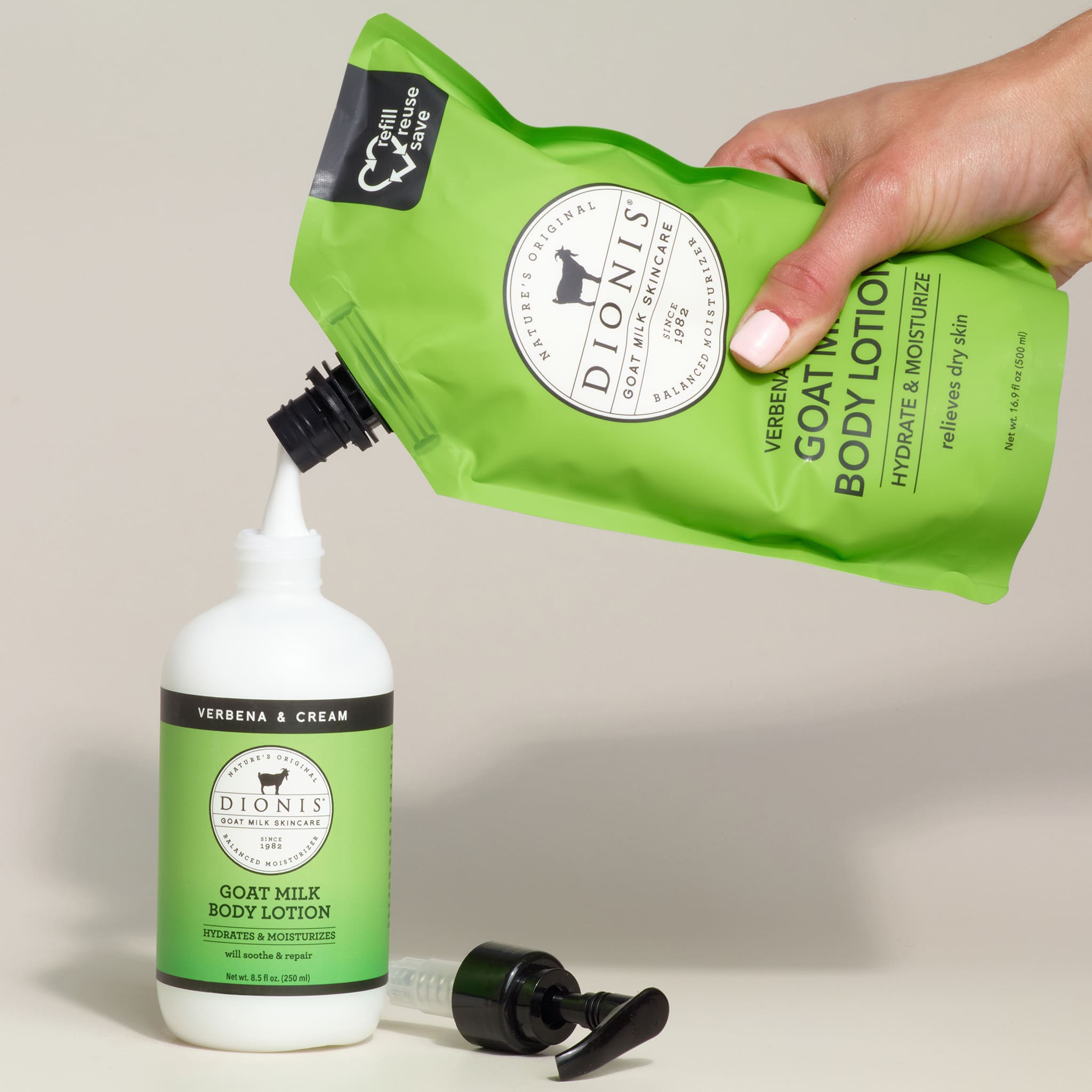 Green Dionis goat milk body lotion being poured from a pump into a bottle on a beige background