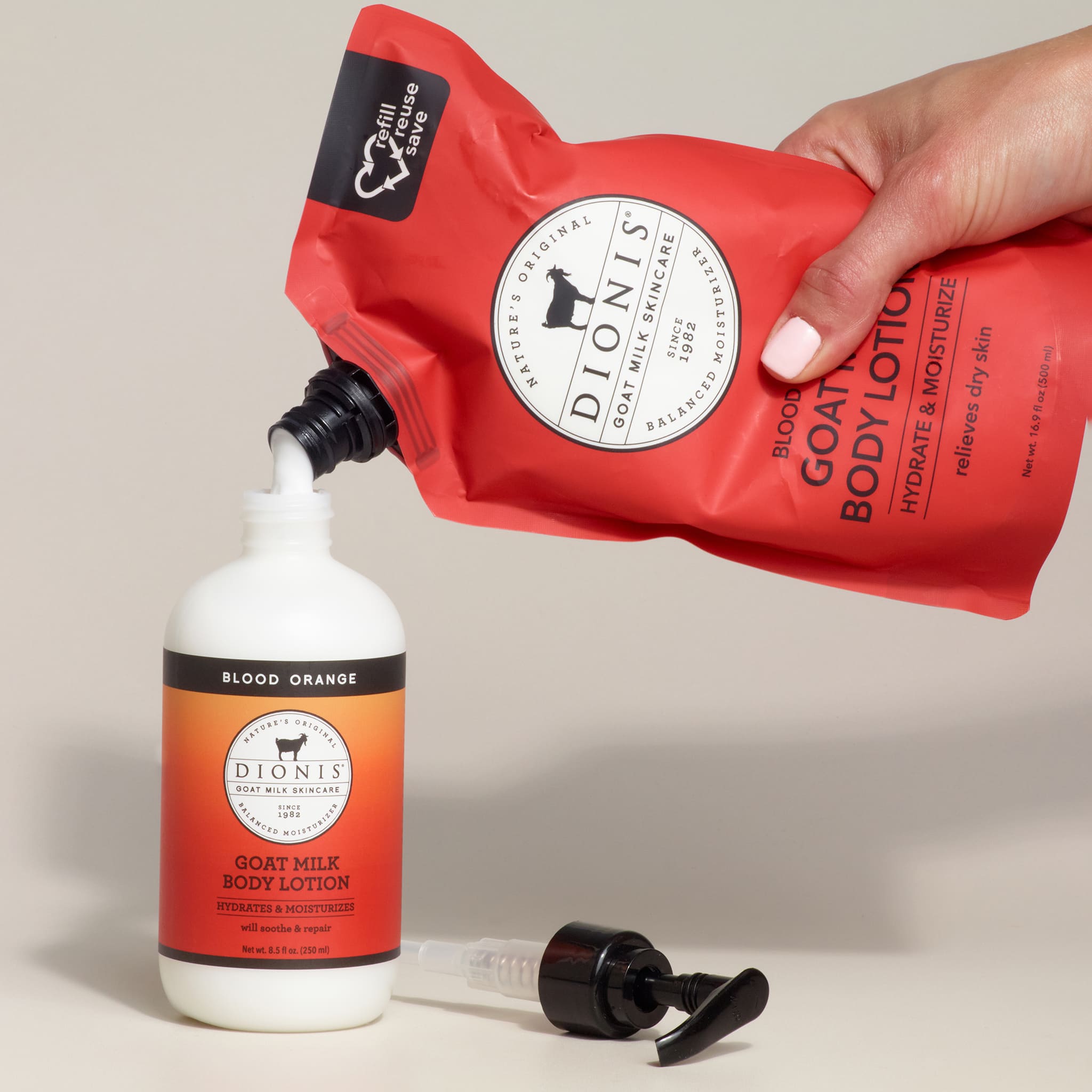 Red Dionis goat milk body lotion pouch being squeezed onto a bottle of blood orange lotion.