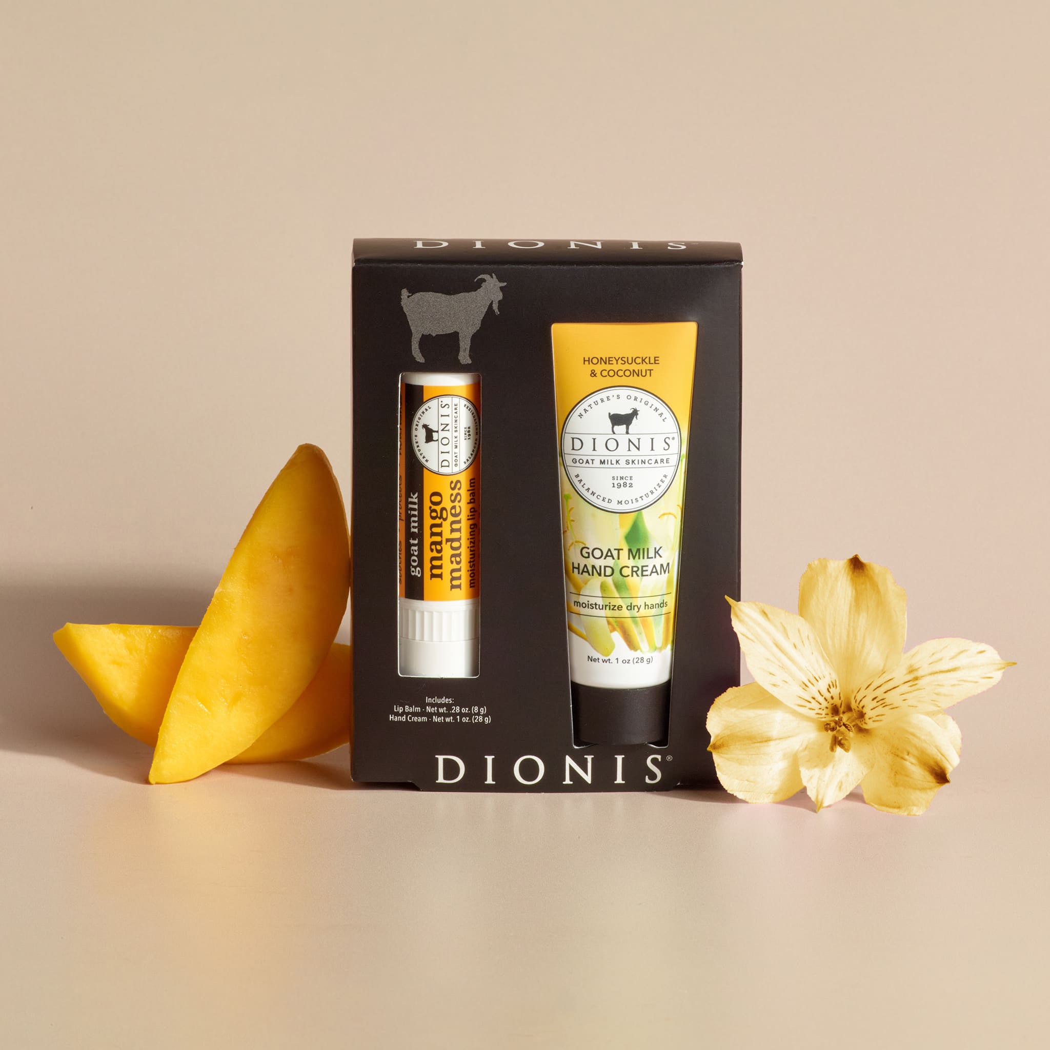 Dionis Goat Milk Skincare Honeysuckle Mango Lip & Hand Set in its packaging next to fragrance props of sliced mango and a honeysuckle flower, against a plain beige background