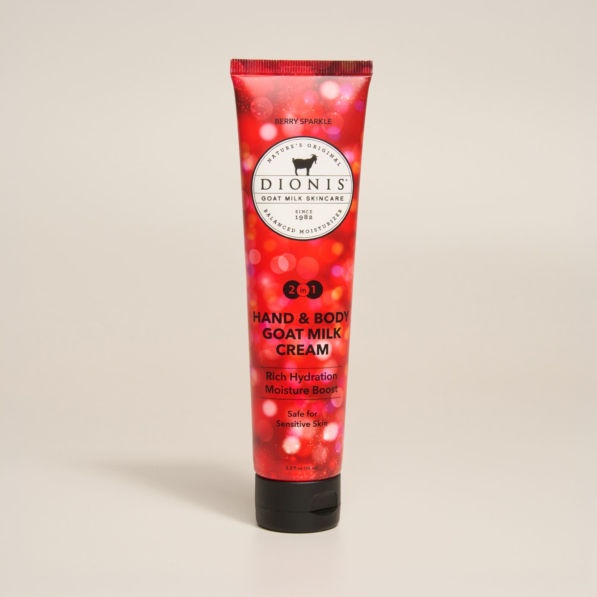 A squeeze tube of Dionis Berry Sparkle Hand & Body Goat Milk Cream. The tube is red with a sparkle pattern and a black cap, set against a solid light beige background.