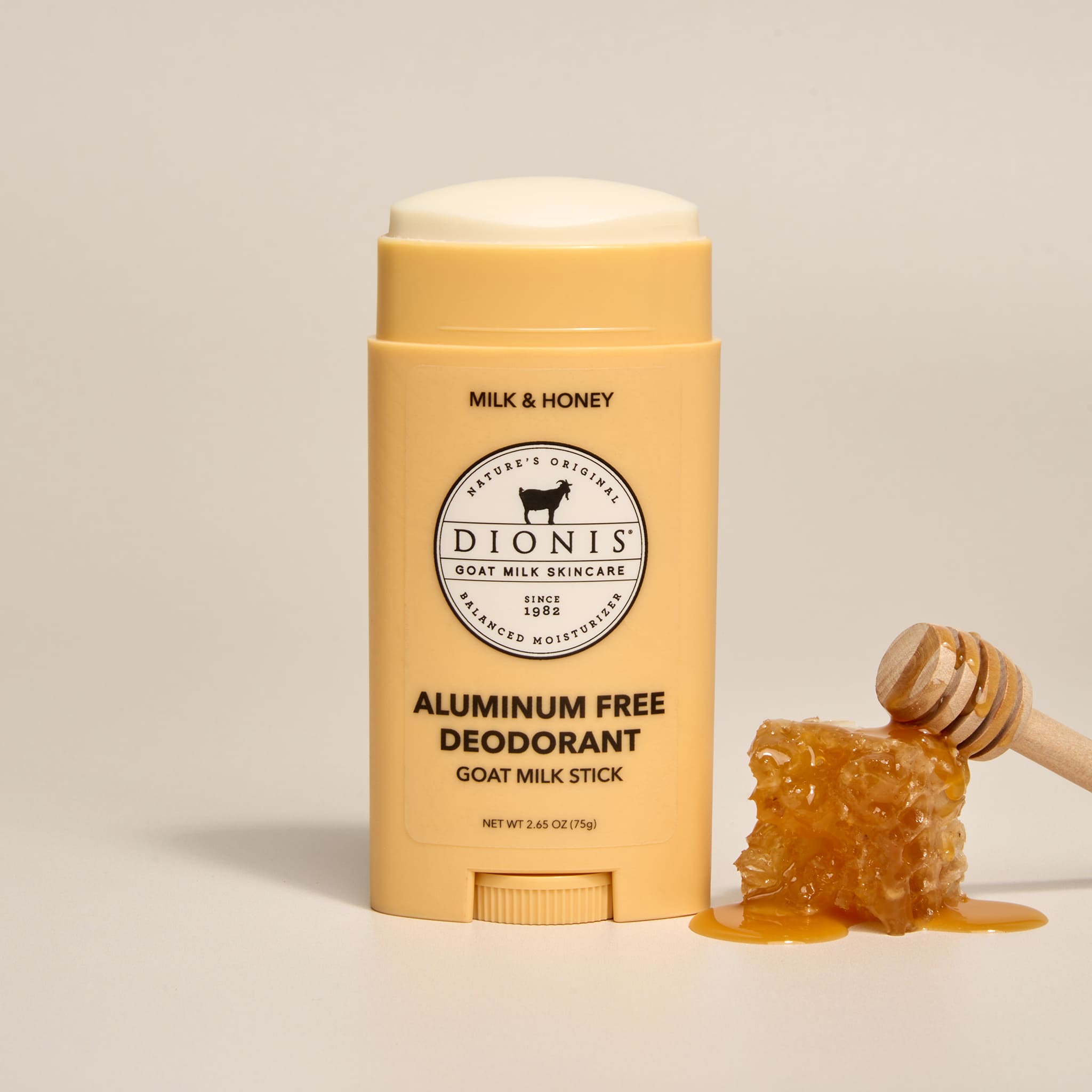 Dionis Milk & Honey aluminum-free goat milk deodorant stick with a honeycomb and honey dipper on a beige background