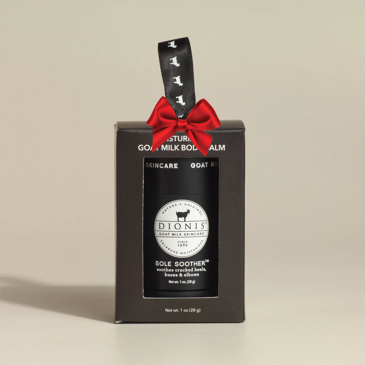 A black gift box for Dionis Sole Soother Goat Milk Body Balm, featuring a black jar with a white circular logo and a black ribbon with goat silhouettes, set against a warm beige background.