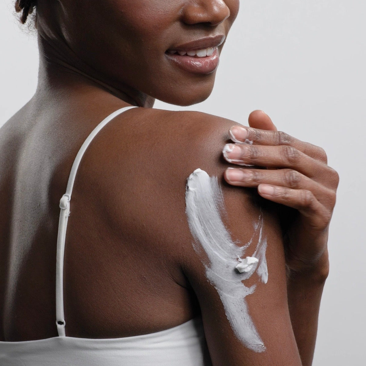 Woman applying body butter to her shoulder with a white background
