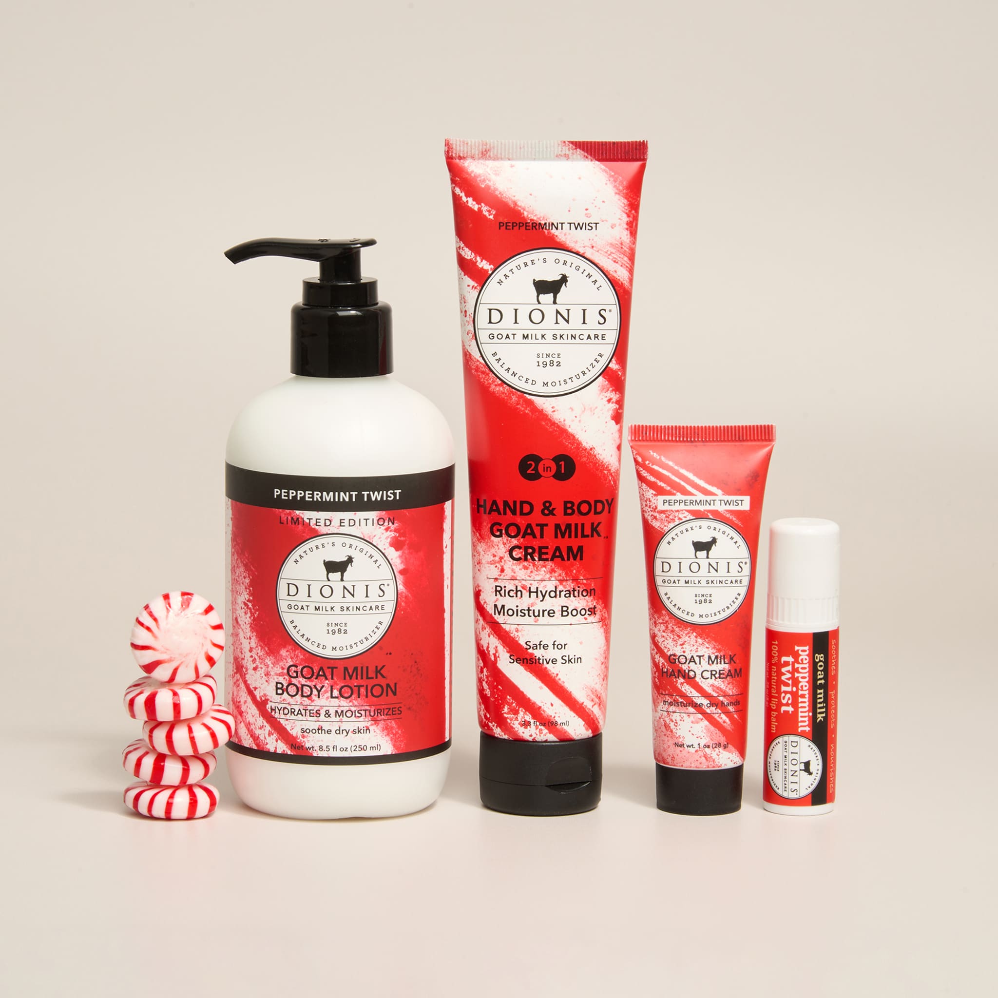 A set of Dionis Body & Beauty products in red, white, and black packaging, including a pump bottle of Peppermint Twist Goat Milk Body Lotion, a 2-in-1 Hand & Body Goat Milk Cream tube, a smaller hand cream tube, and a lip balm tube, arranged with candy canes on a light beige background.
