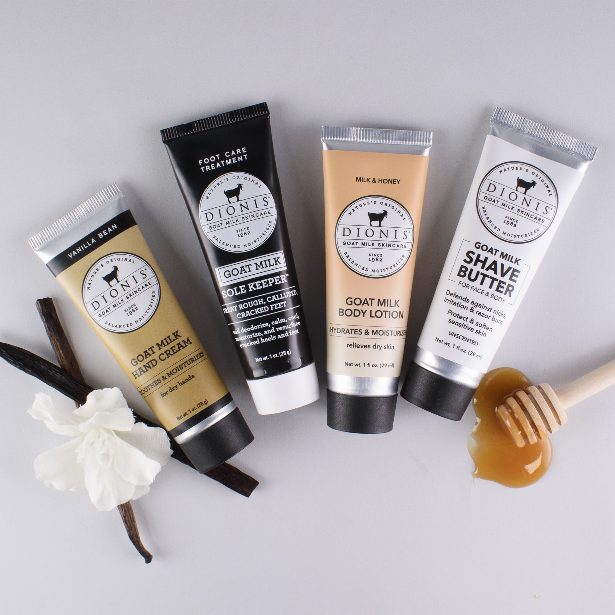 Assorted goat milk bath & body products lined up together, displayed with vanilla and honey accessories