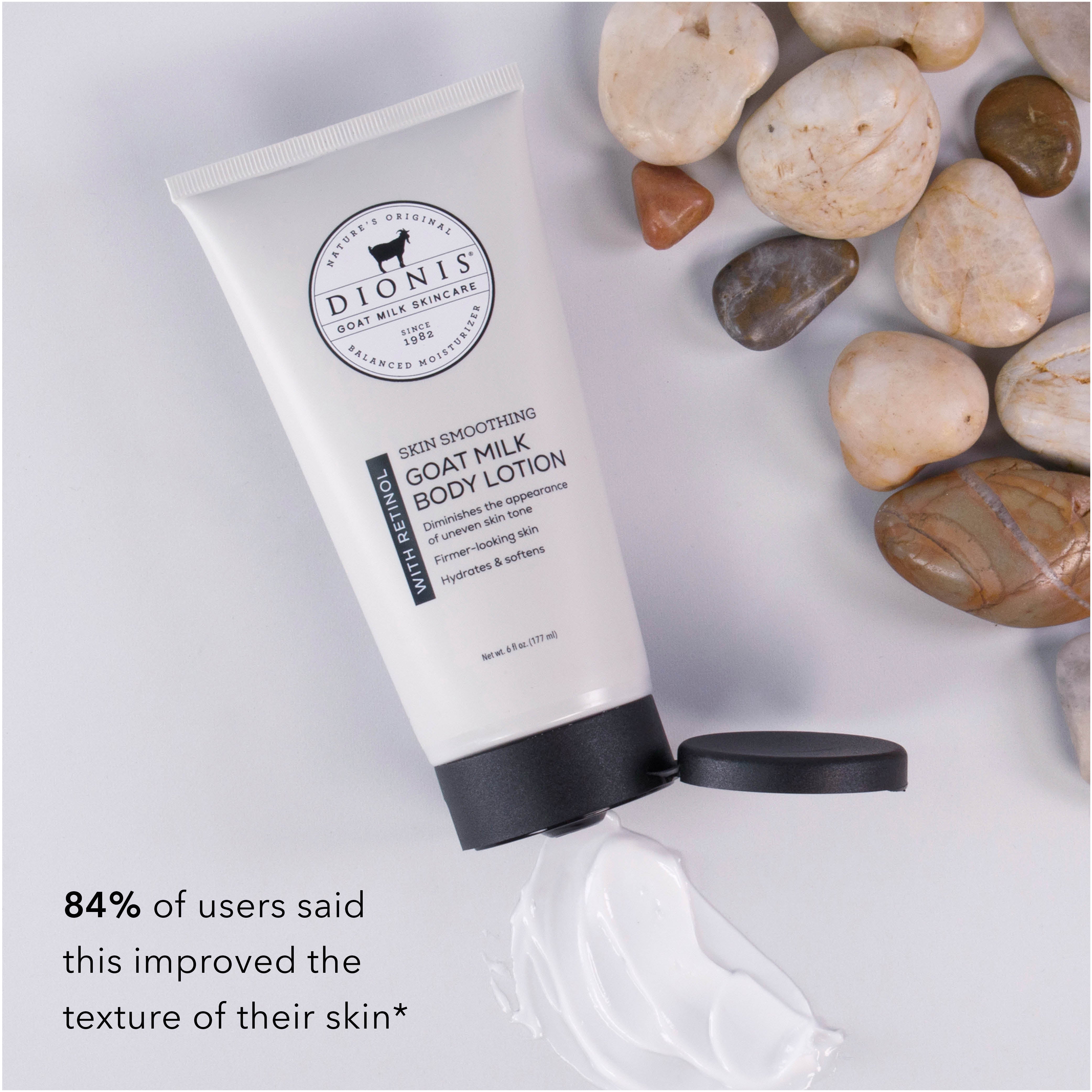 A tube of Dionis Goat Milk Body Lotion with Retinol with its cap off and a dollop of white lotion in front, styled on a light gray surface with decorative stones. Text in the lower left reads: '84% of users said this improved the texture of their skin'.