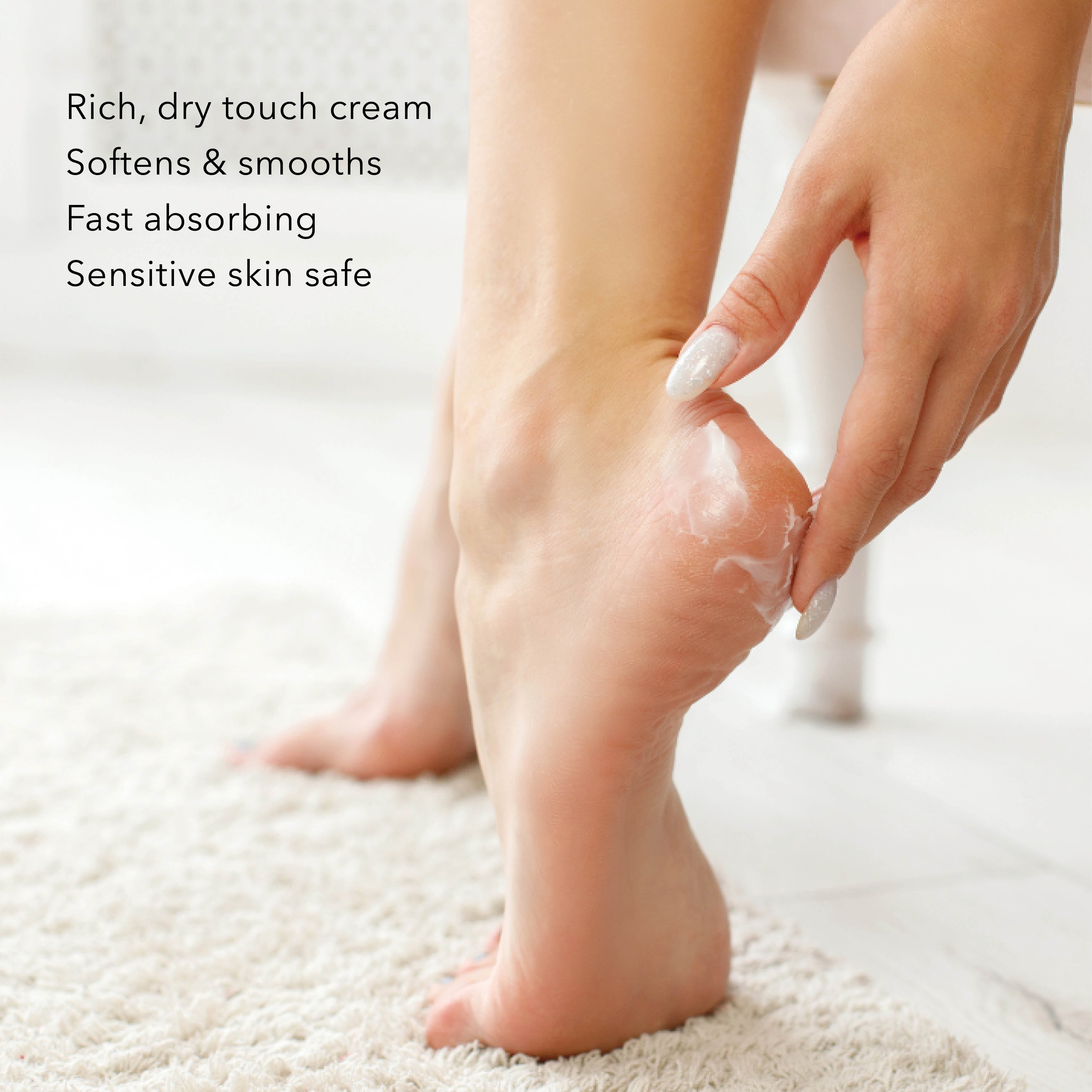 A person applying white cream to the sole of their foot on a textured rug, with text on the left reading 'Rich, dry touch cream Softens & smooths Fast absorbing Fast absorbing Sensitive skin safe'.