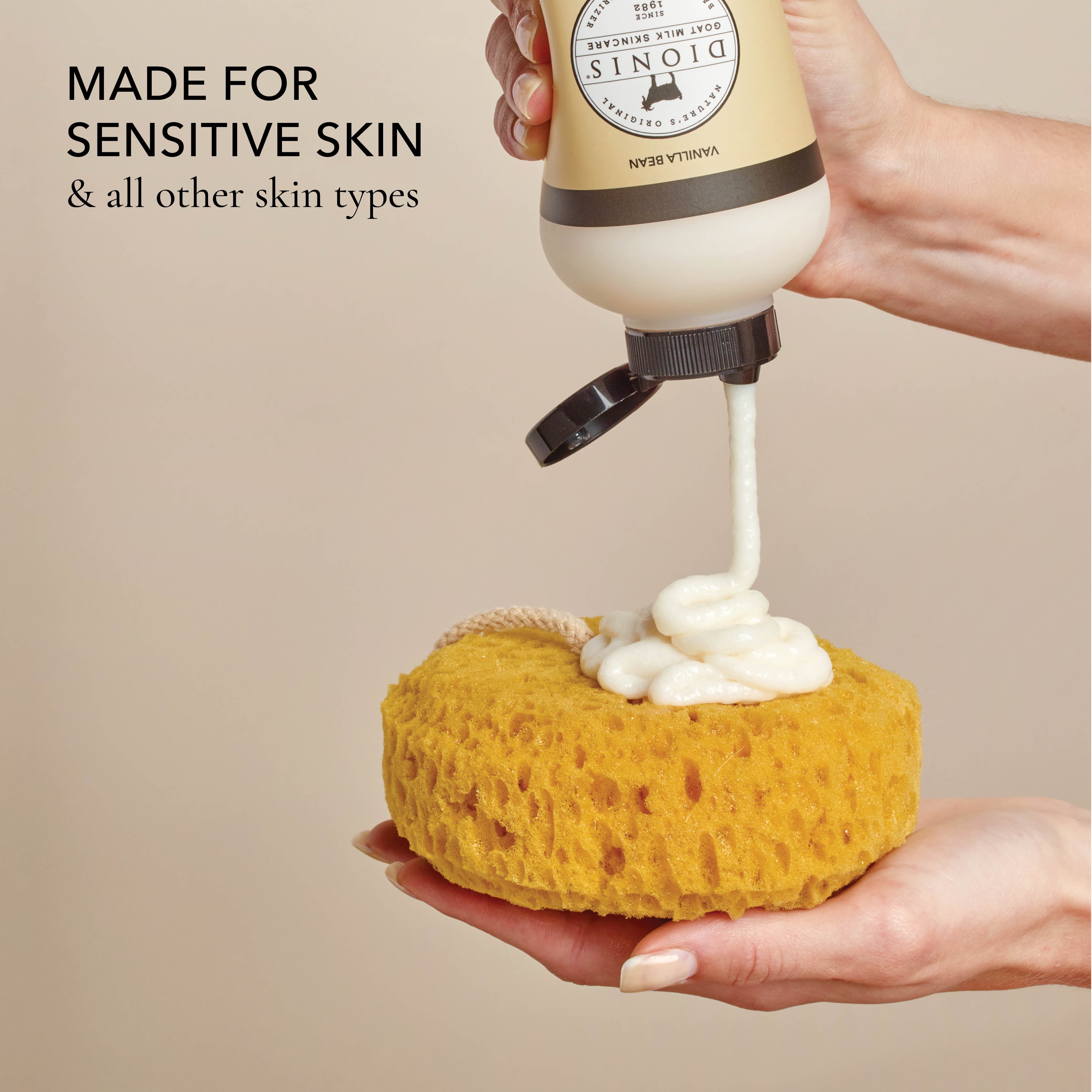 Hand holding a bottle of the shower creme and squeezing it out onto a loofah being held by the other hand, with the text that says "made for sensitive skin & all other skin types", all on a beige background.