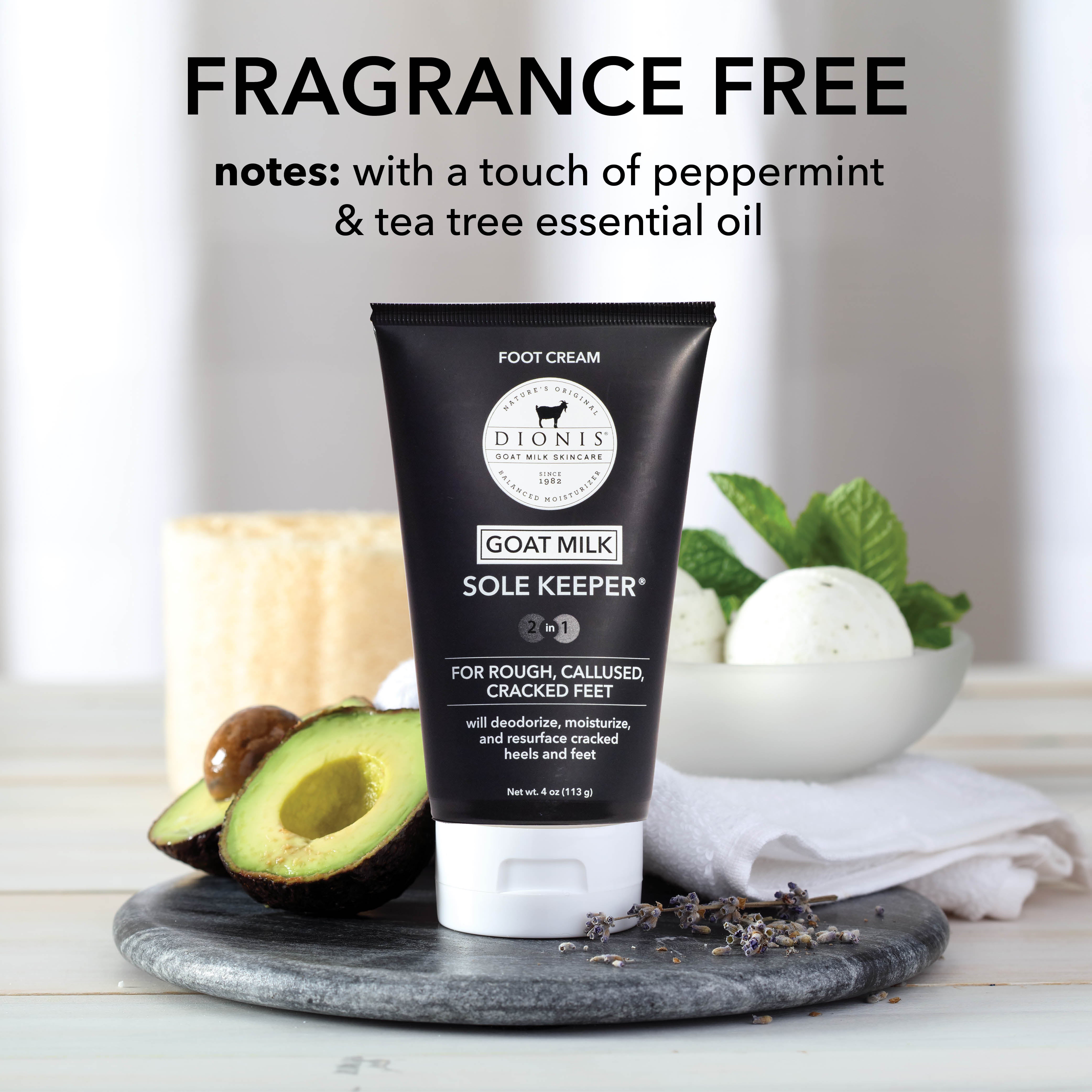 A black tube of Dionis Sole Keeper® foot cream stands on a gray stone tray with avocado halves, dried lavender, a candle, mint, and a white towel in a softly lit setting. Text at the top reads 'FRAGRANCE FREE notes: with a touch of peppermint & tea tree essential oil.