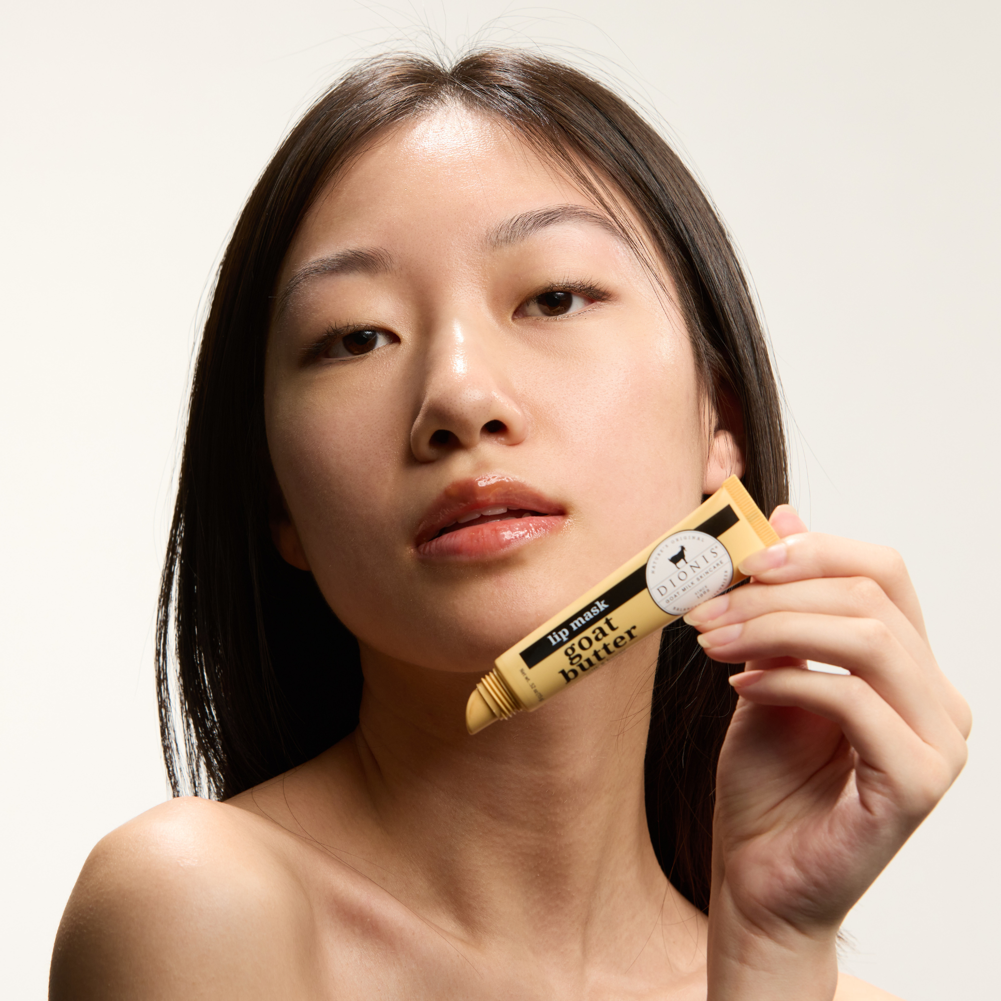 Asian model posing with Dionis Goat Butter Lip Mask in front of her face.