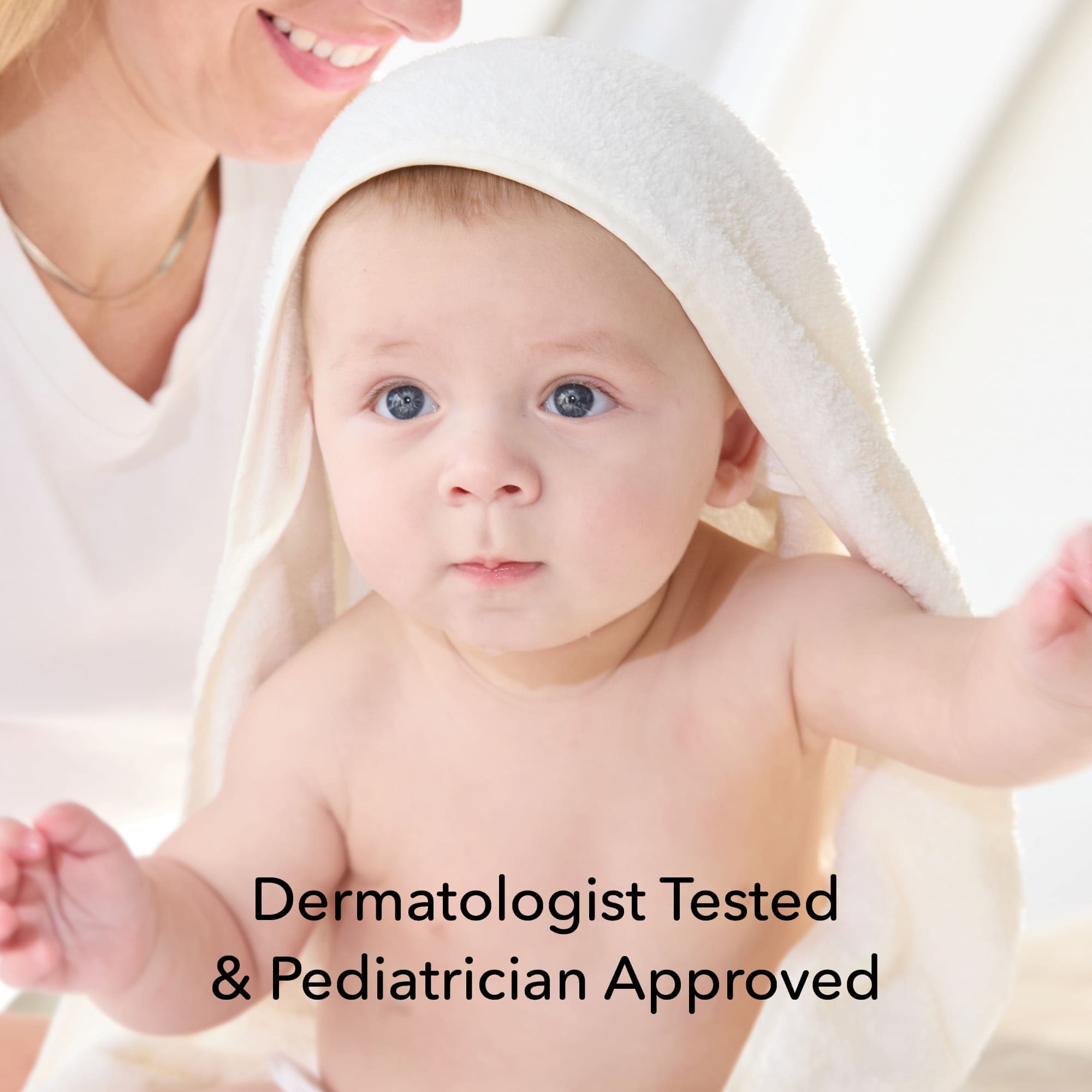 A baby wrapped in a white towel with a hood, looking at the camera, with a woman partially visible in the background. Text overlay reads 'Dermatologist Tested & Pediatrician Approved'.
