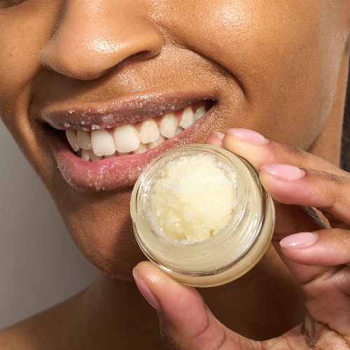 Woman showing the Dionis goat sugar lip polish in the jar and with some on her lips