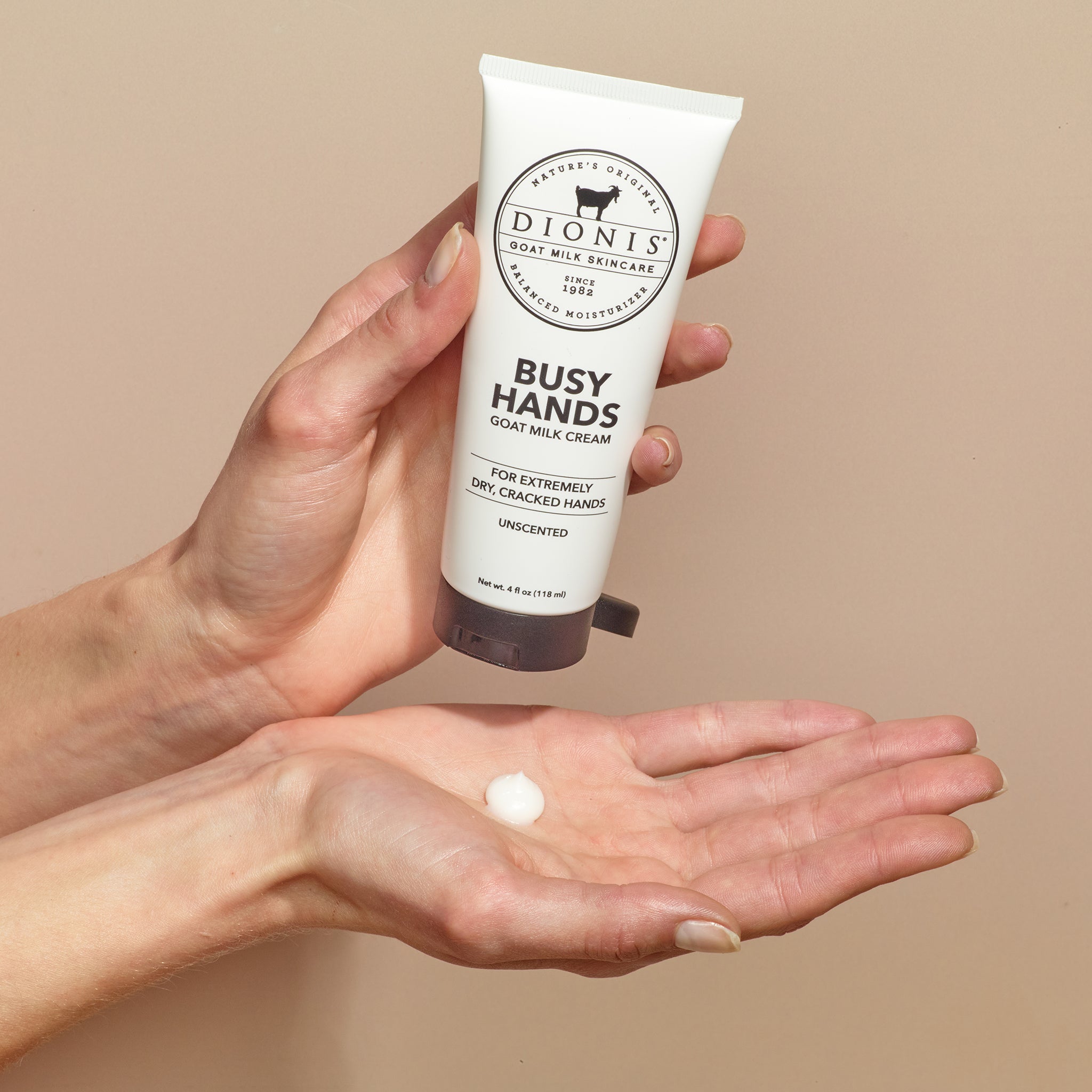 A person holding Dionis Goat Milk Skincare Busy Hands Hand Cream in one and with a dollop of the hand cream in the palm of their other hand which is held out under the tube of hand cream.