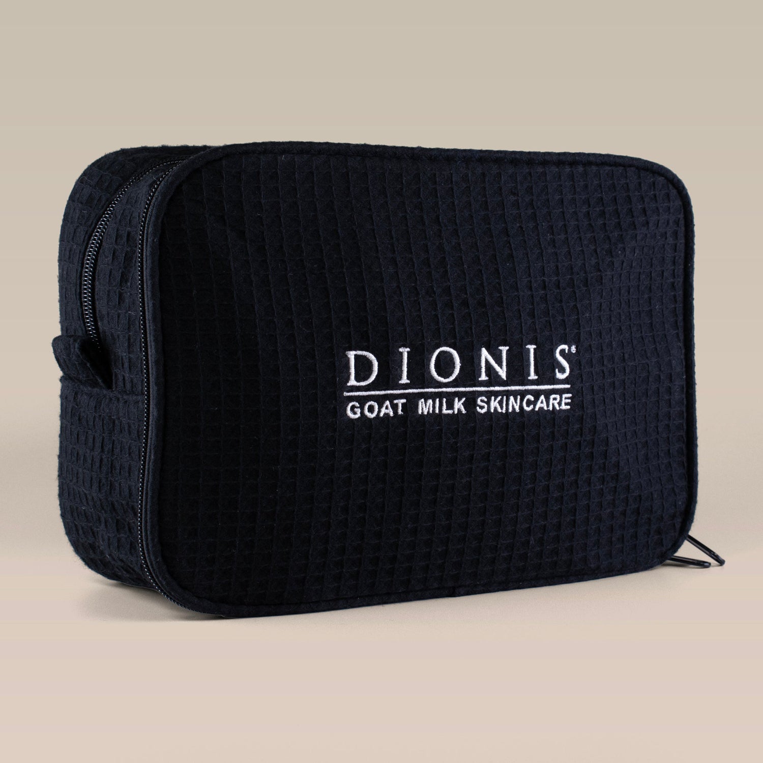 Black textured toiletry bag with 'Dionis Goat Milk Skincare' branding and a zipper top on a beige background