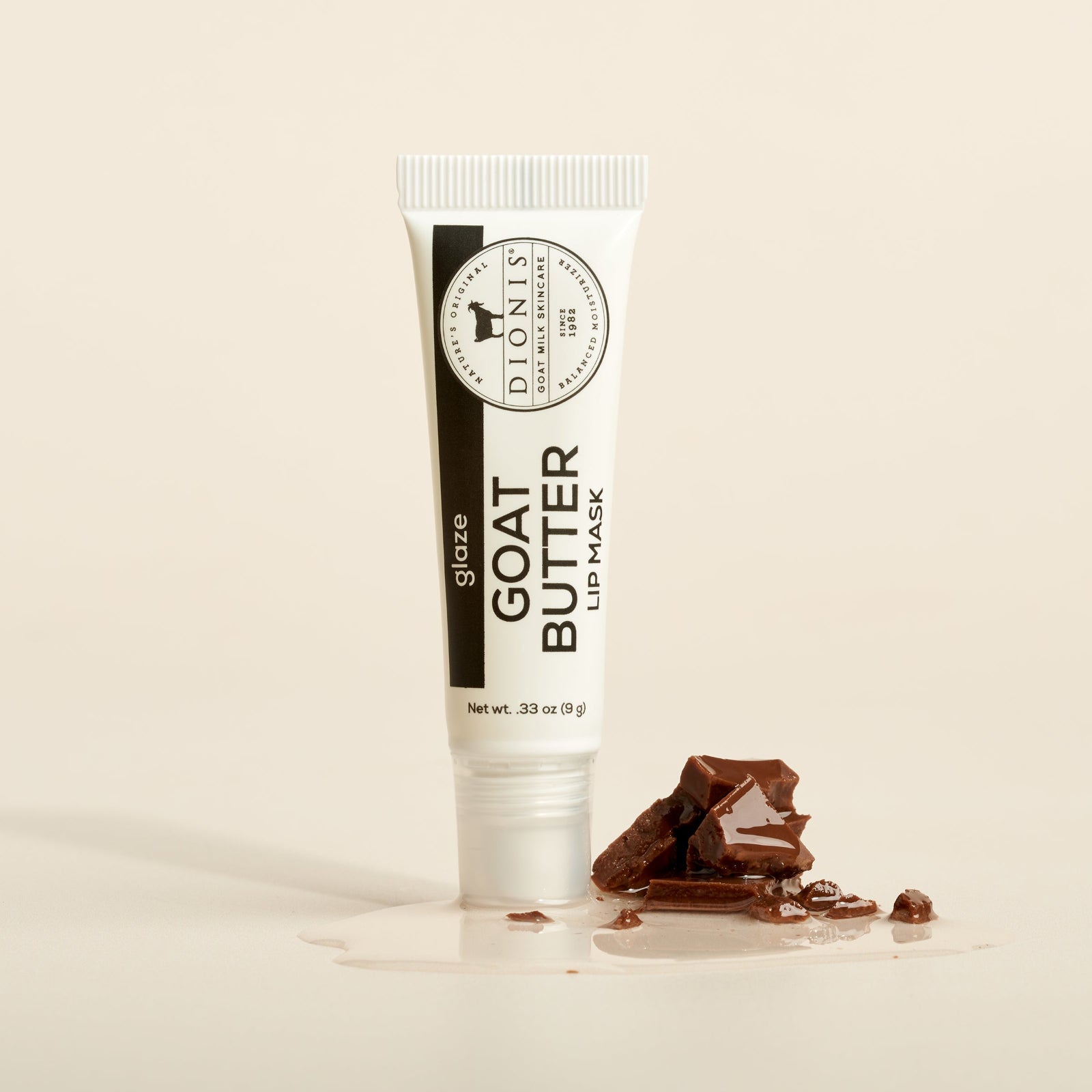 Dionis Goat Milk Skincare 0.33 oz Glaze Goat Butter Lip Mask with chocolate and sugary glaze as props on a beige background
