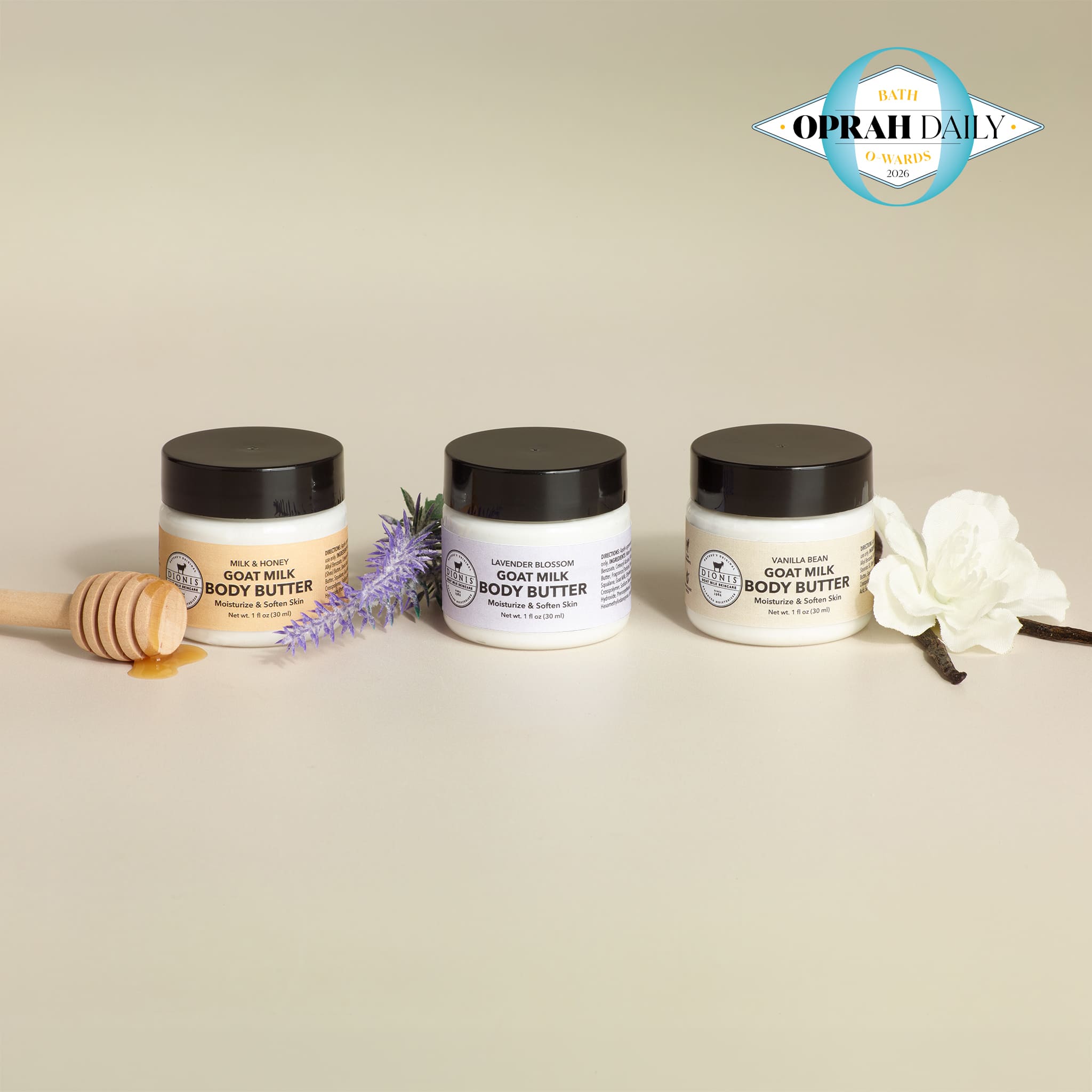 Three 1 oz jars of Dionis body butter in a line with a honey dipper and flower props on a beige background, featuring the Oprah Daily Bath O-wards logo.