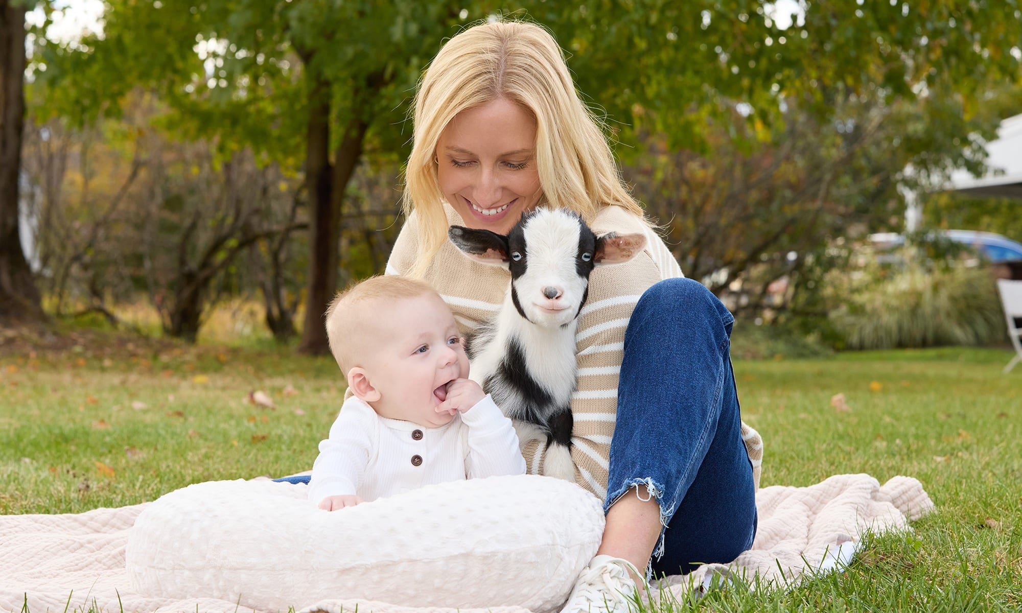 Mom and baby with a young goat on a blanket in a park setting