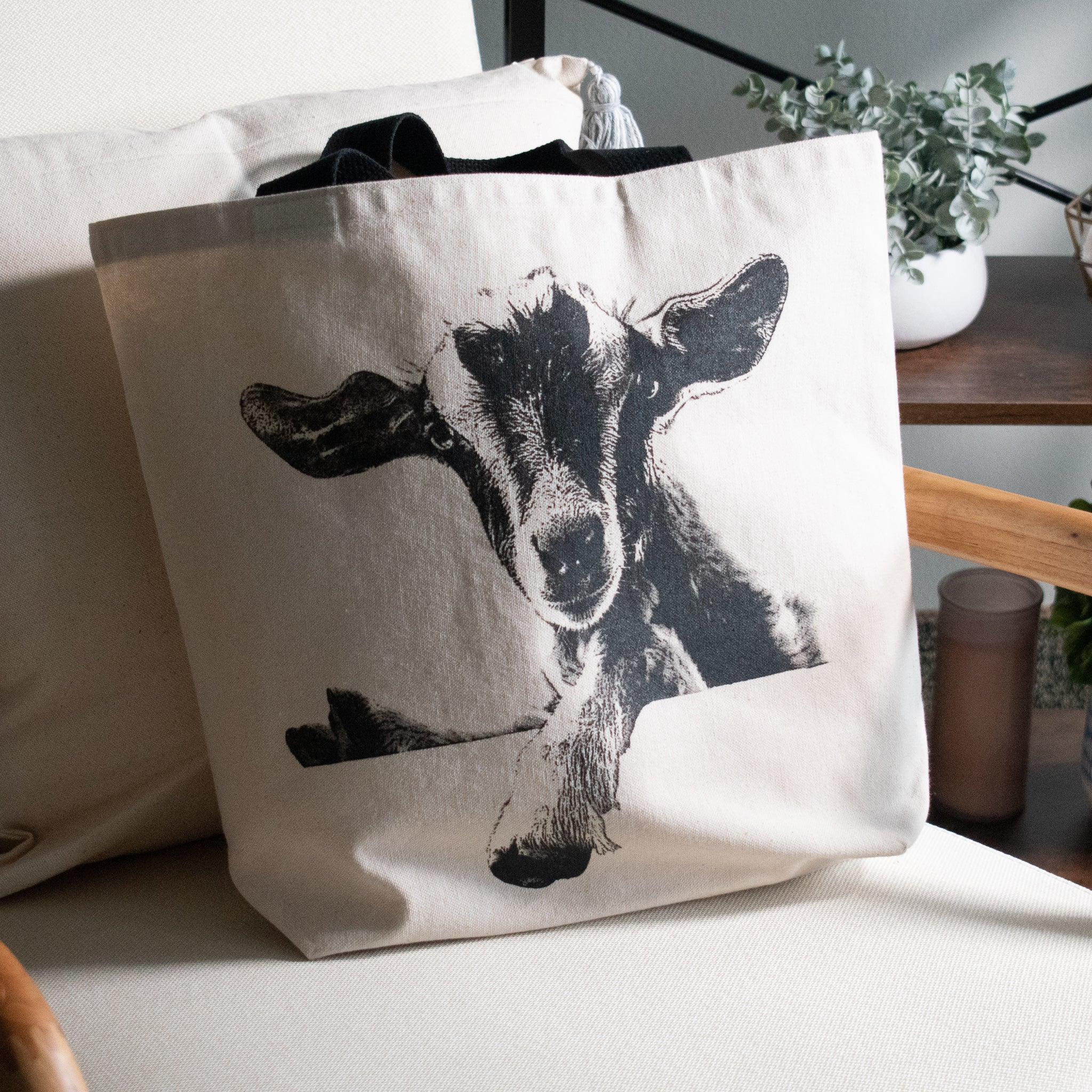 Canvas shopping tote with a black and white goat printed on it sitting on a chair