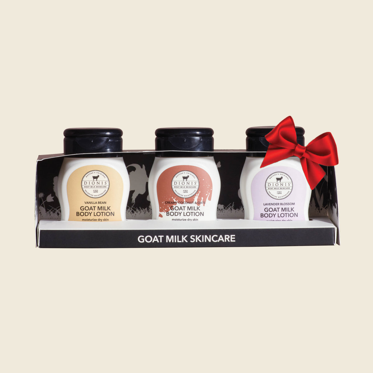 Three small goat milk body lotion bottles in a clear-front display box. The bottles have black caps and labels in three fragrances: Vanilla Bean Creamy Coconut & Oats, and Lavender Blossom. Shown with a red bow.
