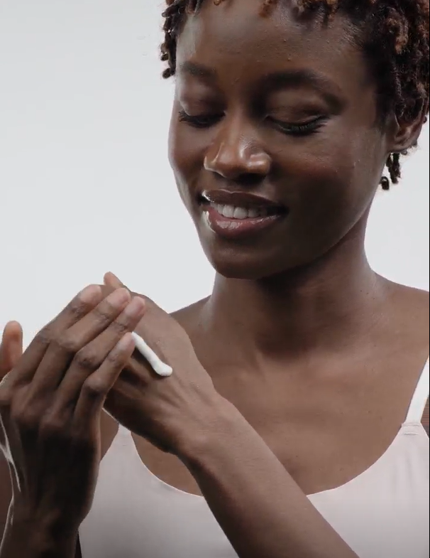 Woman applying cream to her hand against a plain background