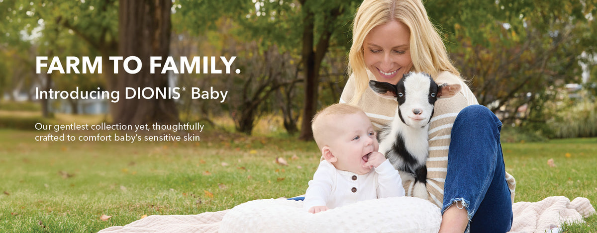 A promotional outdoor photo shows a smiling woman sitting on grass with a baby and a black-and-white goat. Large text reads 'FARM TO FAMILY. Introducing DIONIS Baby - Our gentles collection yet, thoughtfully crafted to comfort baby's sensitive skin.'