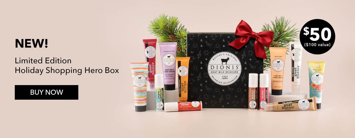 Dionis Goat Milk Skincare's Limited Edition Holiday Shopping Hero Box set, featuring a black gift box with a red bow, surrounded by various body care and lip products on a beige background with promotional text that reads "NEW! Limited Edition Holiday Shopping Hero Box. Buy Now"