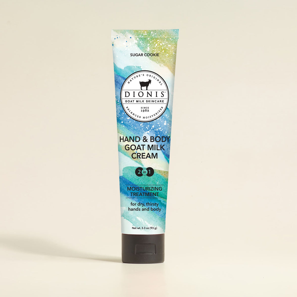 A tube of Dionis Hand & Body Goat Milk Cream in the 'Sugar Cookie' scent, featuring a colorful blue, green, and gold watercolor design with a black cap, set against a plain beige background.