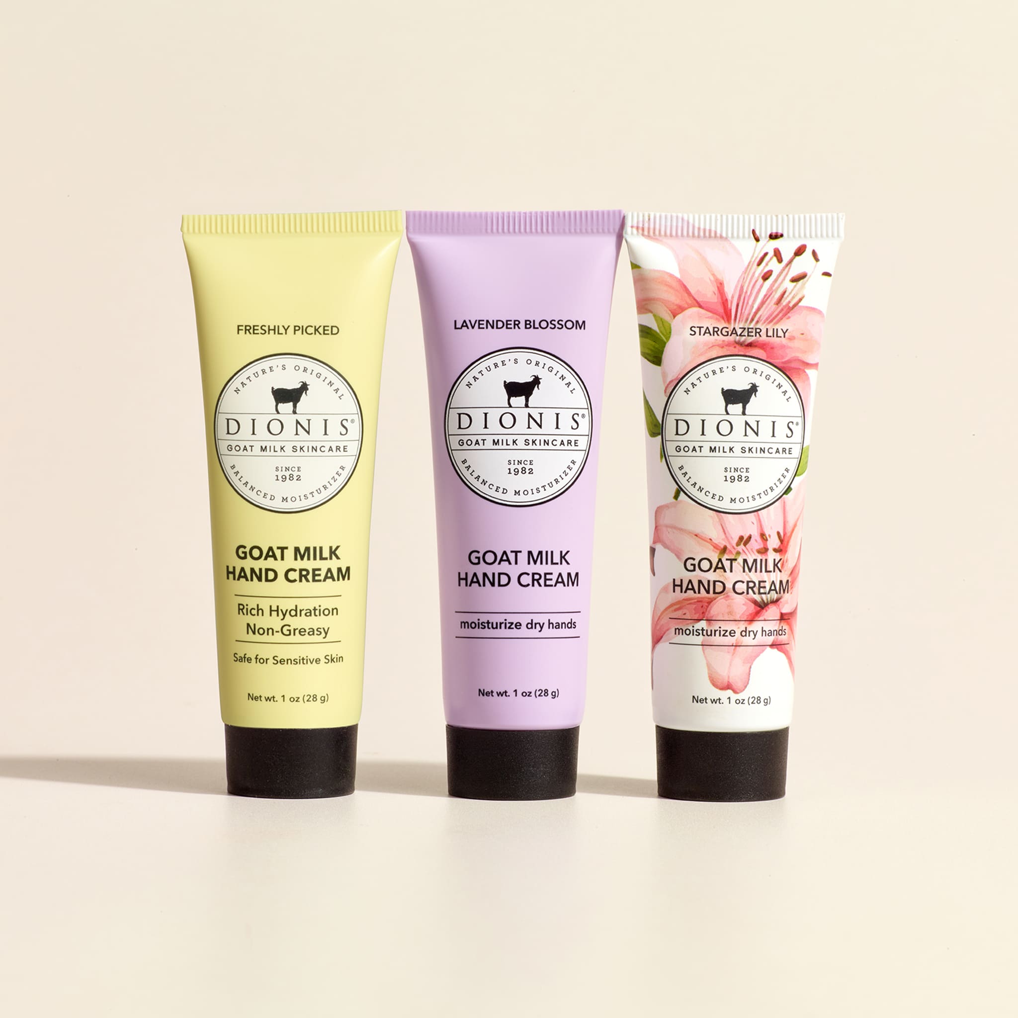 1 tube each of Dionis Goat Milk Skincare Freshly Picked Hand Cream, Lavender Blossom Hand Cream, and Stargazer Lily Hand Cream lined up horizontally against a beige background