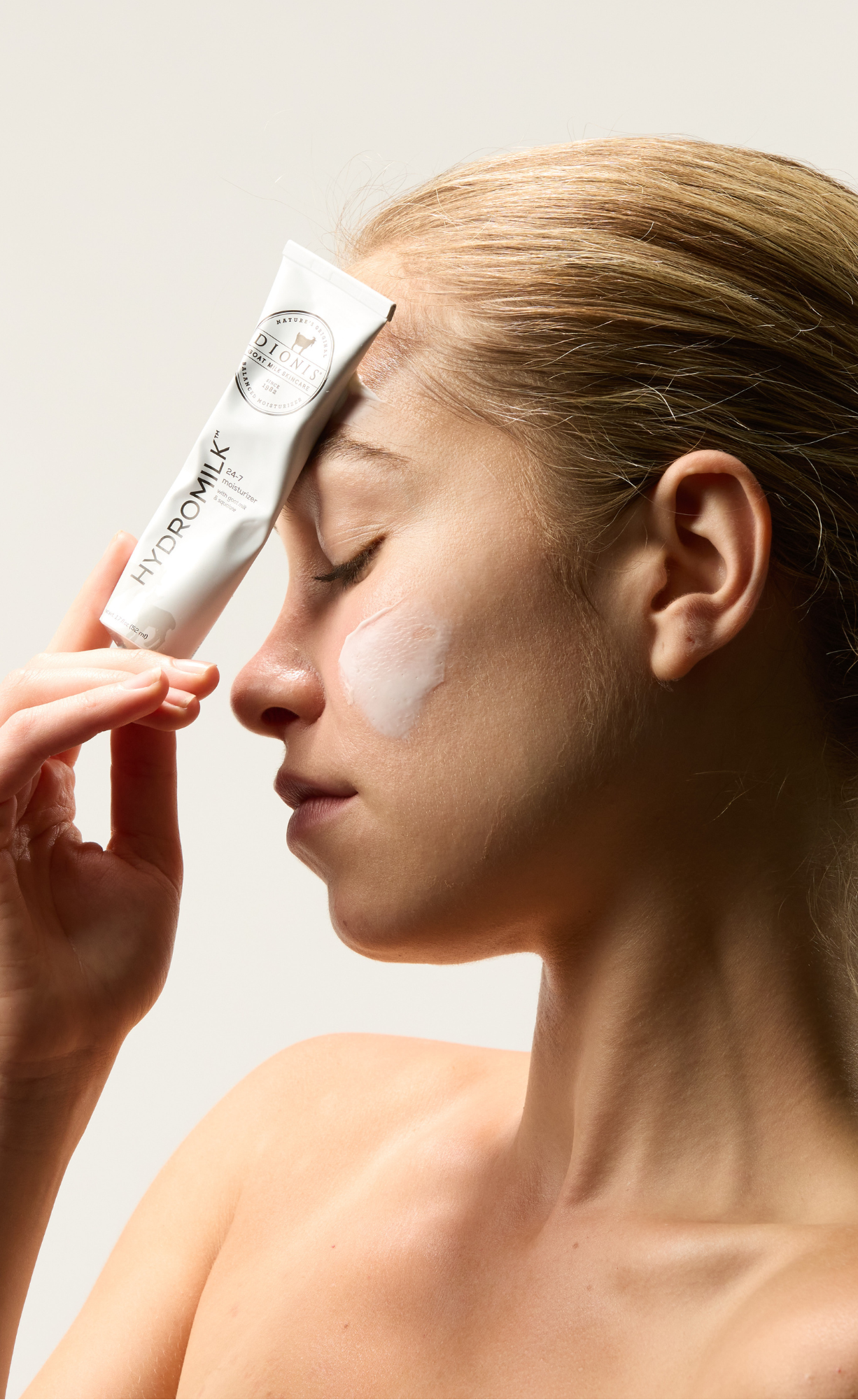 woman holding hydromilk to her face with a swatch of the moisturizer on her cheek