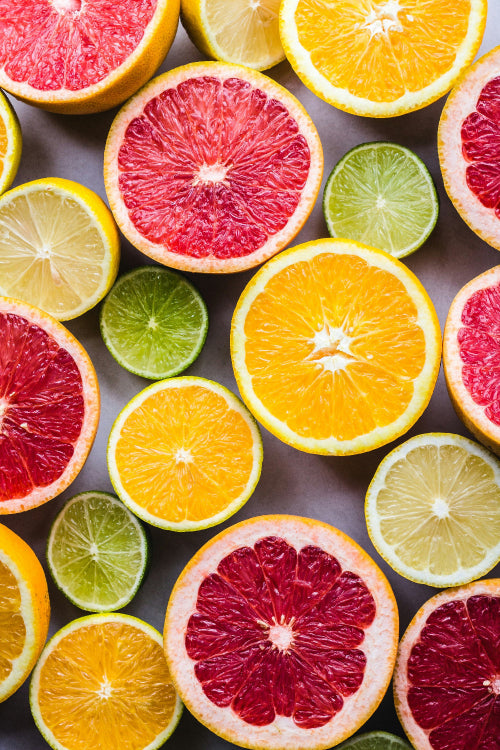 Assorted citrus fruits including grapefruits, oranges, and limes on a gray background