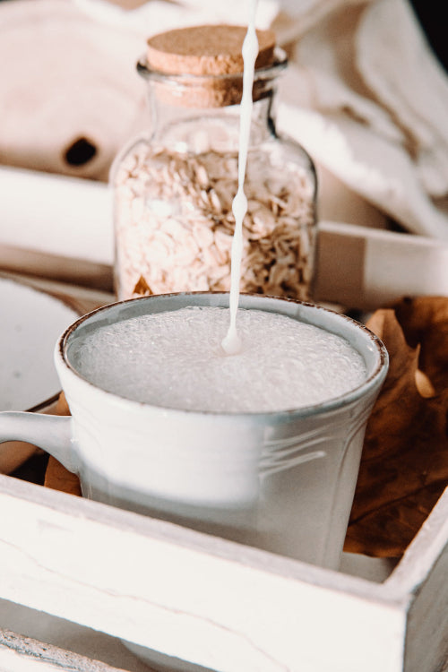 Glass jar of oatmeal being poured into a mug with a white background