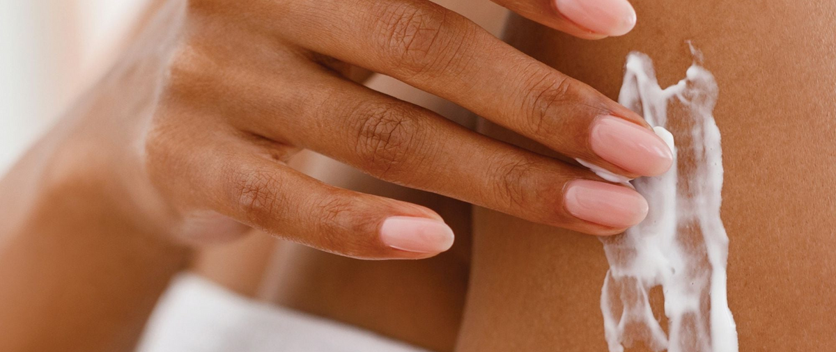 Close up of model applying body cream to her skin.