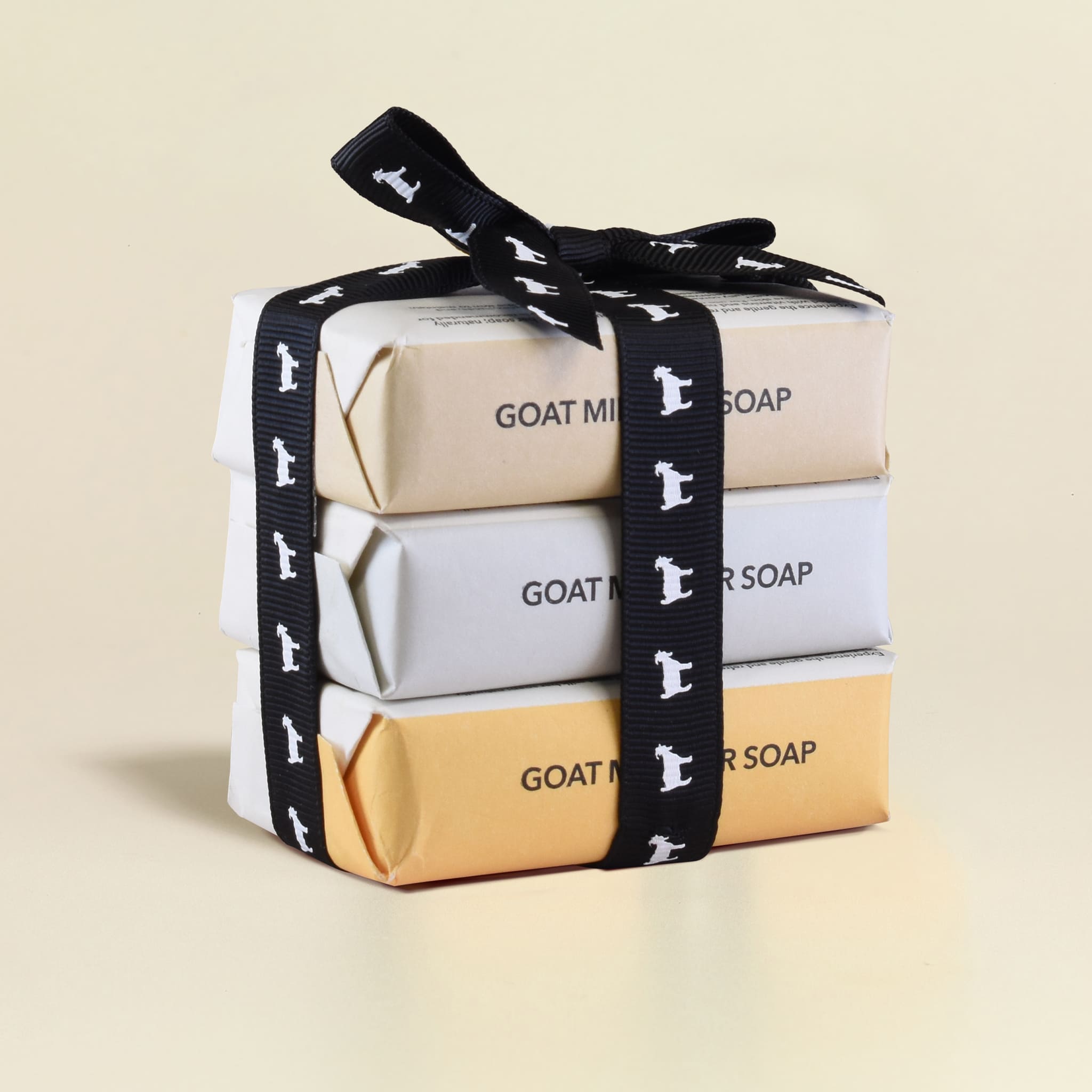 Three bars of goat milk soap stacked on top of each other with a black and white goat silhouette ribbon on a beige background.