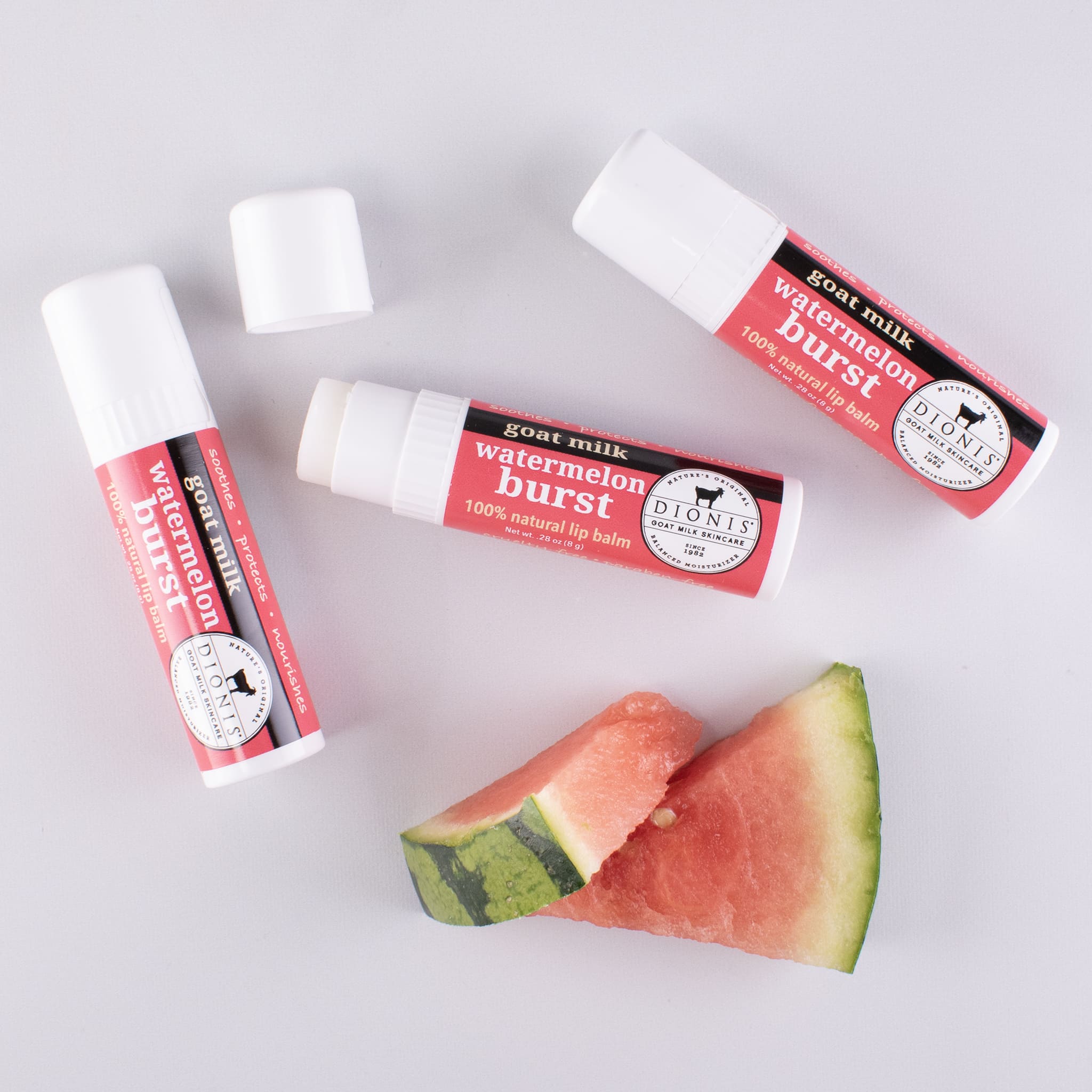 3 Watermelon Burst goat milk lip balms displayed with 2 pieces of fresh watermelon