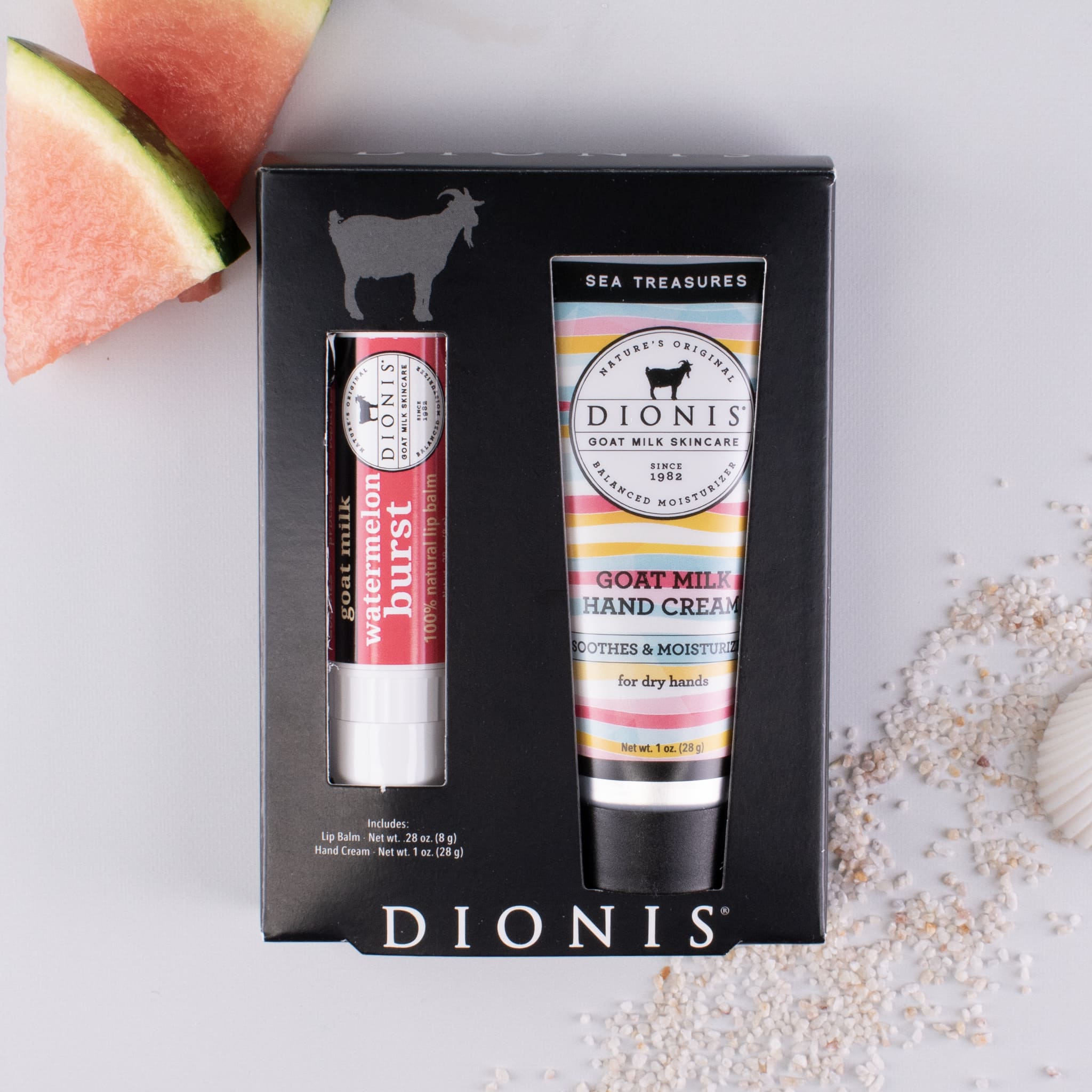 Watermelon Burst goat milk lip balm and Sea Treasures goat milk hand cream in a black box together, with watermelon slices and sand accessories